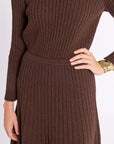 Close up of woman wearing a brown ribbed knit skirt and matching long sleeve top on a white background