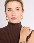 Close up of woman with hand on shoulder in gold jewelry and ribbed knit brown sleeveless turtleneck top