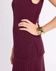 Close up of woman with hand on hip wearing ribbed knit burgundy sleeveless top with matching skirt and gold bracelet against a white background