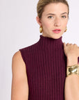 Close up of woman with hand on shoulder wearing a ribbed knit burgundy sleeveless top against a white background