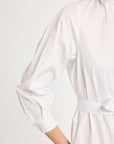 A close-up shot focusing on the sleeve, cuff, and belted waist of the white shirt dress. The model's hands are obscured as they rest in the pockets, highlighting the crisp Italian cotton fabric.