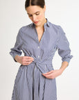 A woman in a navy and white striped shirt dress with a matching sash tied at the waist.