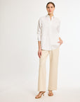 A woman wearing a white, long-sleeved, button-up shirt with a collar and beige pants.