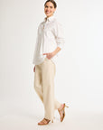A woman wearing a white, long-sleeved, button-up shirt with a collar and beige pants.