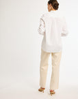 A woman wearing a white, long-sleeved, button-up shirt with a collar and beige pants.