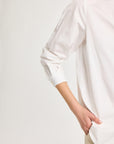 Close up of one sleeve of a long-sleeved white shirt with hand in pant pocket.