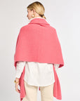 Person wearing a pink cape over a white shirt and beige pants on a light gray background