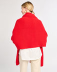Person wearing a red shawl over a white shirt and beige pants on a light gray background