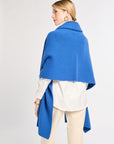 Woman wearing a blue cape over a white shirt and beige pants on a light gray background