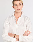 Woman wearing a white shirt with a pearl necklace against a plain background