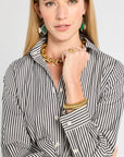 Woman wearing a black and white striped shirt with gold jewelry on a plain background