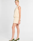 Woman wearing a beige sleeveless top and shorts with green shoes on a white background