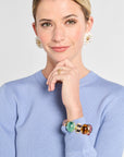 Woman wearing a blue sweater with a colorful bracelet on her wrist, against a plain background.