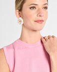 Woman wearing a pink sleeveless top with floral earrings and a ring on a light gray background