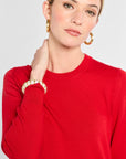 Woman wearing a red sweater with gold jewelry on a plain background