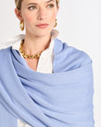Woman wearing a light blue scarf, white shirt, and gold necklace on a white background