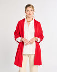 Woman wearing a red cardigan over a white shirt and beige pants on a white background