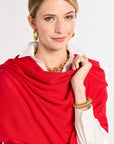 Woman wearing a red scarf, white shirt, and gold jewelry on a plain background