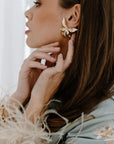 A medium close-up of a woman's profile wearing large, gold-toned, floral earrings.