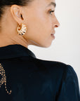 A profile shot of a woman's face and shoulder wearing large, gold-toned, Stud Earrings and a dark navy top with a metallic animal print on the shoulder.