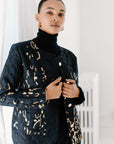 A person wearing a black blazer with gold jacquard pattern and ostrich feather details.