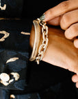 A wide, polished gold oval link bracelet with a repeating pattern shown on a wrist.