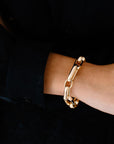 A gold link bracelet with a wide paperclip design, displayed on a wrist.