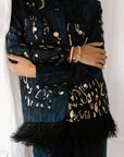 A person wearing a black blazer with gold jacquard pattern and ostrich feather details.