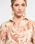 Woman wearing a patterned blouse with gold earrings on a light background