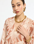 Woman wearing a patterned top and gold jewelry on a white background