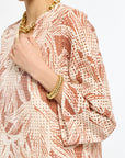 Person wearing a patterned top with gold jewelry on a white background