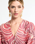 Woman wearing a pink and white patterned dress with gold earrings on a light background