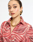 Woman wearing a red patterned shirt with gold jewelry on a white background