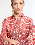 Woman wearing a red and white patterned blouse with gold earrings and bracelet on a light gray background