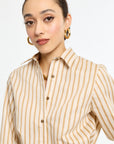 Woman wearing a beige and white striped shirt with gold earrings on a white background