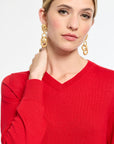 Woman wearing a red sweater and gold earrings on a white background