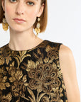 Woman wearing a black dress with gold floral embroidery and gold earrings on a white background