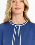 Woman wearing a blue top with white trim on a plain background