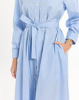 Woman wearing a blue and white striped dress with a belt, standing against a light background.