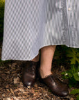 Person wearing a striped dress and brown shoes standing in a garden.
