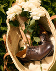 Brown dress shoes in a woven basket with white flowers and green leaves on a natural background