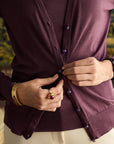 Person wearing a purple cardigan buttoning it up with a blurred background