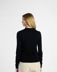 Back of woman wearing a black silk cardigan and beige pants on a white background