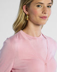 up close shot of a woman wearing a pink silk cardigan with a plain background