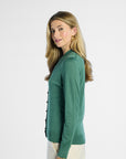 side profile of a woman wearing a green sweater with black buttons on a white background