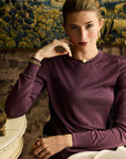 Woman in a purple sweater sitting in a decorative room with tapestries.