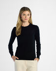 Woman wearing a black long-sleeve top and beige pants on a white background