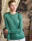 Woman wearing a green sweater in an indoor setting with patterned wallpaper.