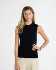 Woman wearing a black sleeveless silk top and beige pants on a white background