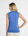 back profile of a woman wearing a blue sleeveless silk top with beige pants on a white background